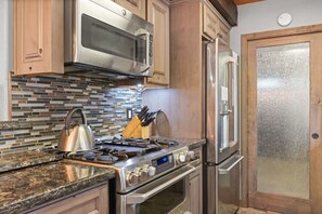 A kitchen with a stainless steel stove, microwave, and refrigerator, a tiled backsplash, and wooden cabinets.