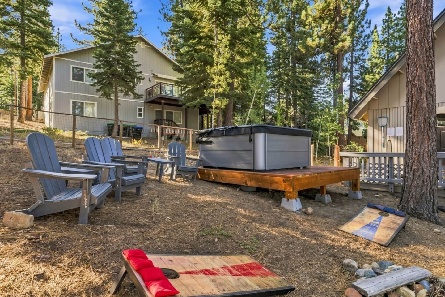 Ein Garten mit Adirondack-Stühlen, einer Feuerstelle und einem Whirlpool auf einer Holzterrasse.