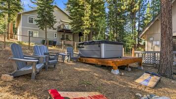 Ein Garten mit Adirondack-Stühlen, einer Feuerstelle und einem Whirlpool auf einer Holzterrasse.