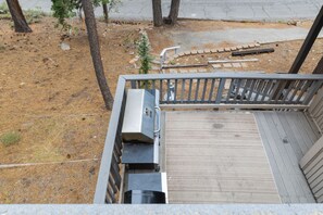 A wooden deck with a grill and a small tree.
