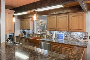 Una cocina con encimeras de granito, armarios de madera, un lavamanos de acero inoxidable e iluminación colgante.