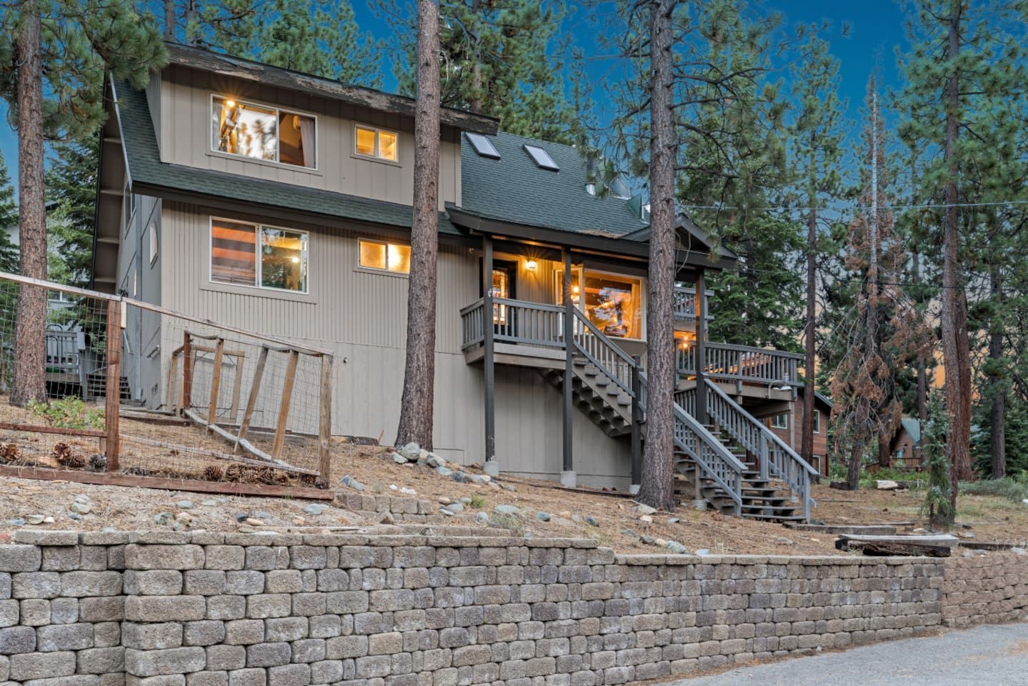 A two-story house with a stone retaining wall, a wooden deck, and a staircase leading to a balcony.