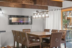 Un comedor con mesa de madera y sillas de cuero, una lámpara colgante y un amplio ventanal con cortinas.