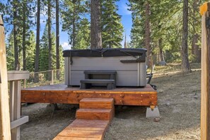 Une terrasse en bois dotée d’un foyer intégré et d’un espace salon, le tout entouré d’une forêt.