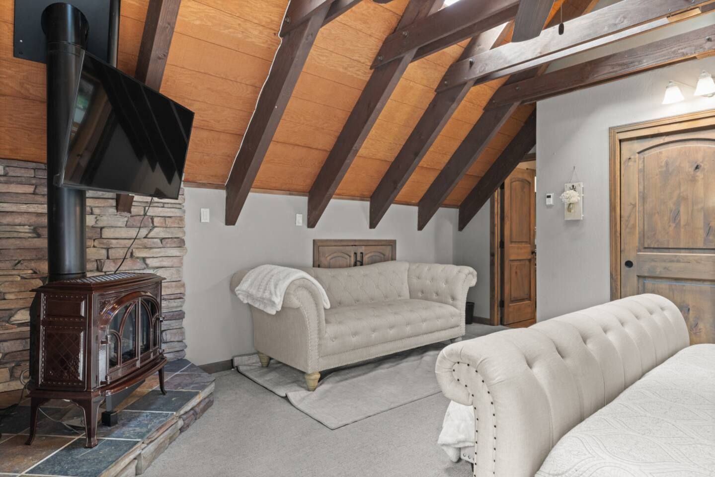 A room with a fireplace, a sofa, a television, and a wooden ceiling.