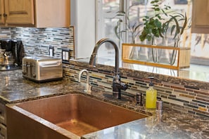 Una cocina con un lavamanos de acero inoxidable, un tostador y una salpicadera con mosaicos.