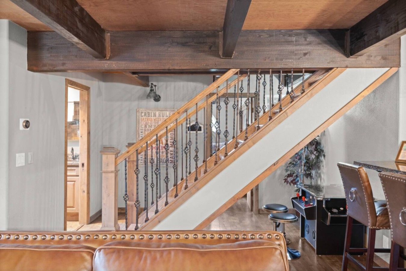 A staircase with a wooden handrail and metal balusters, leading to a room with a dining area featuring a bar and leather seating.