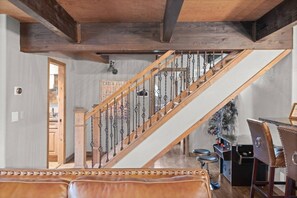 Una escalera con barandilla de madera y balaustradas de metal que conduce a una habitación con comedor, barra y asientos de cuero.