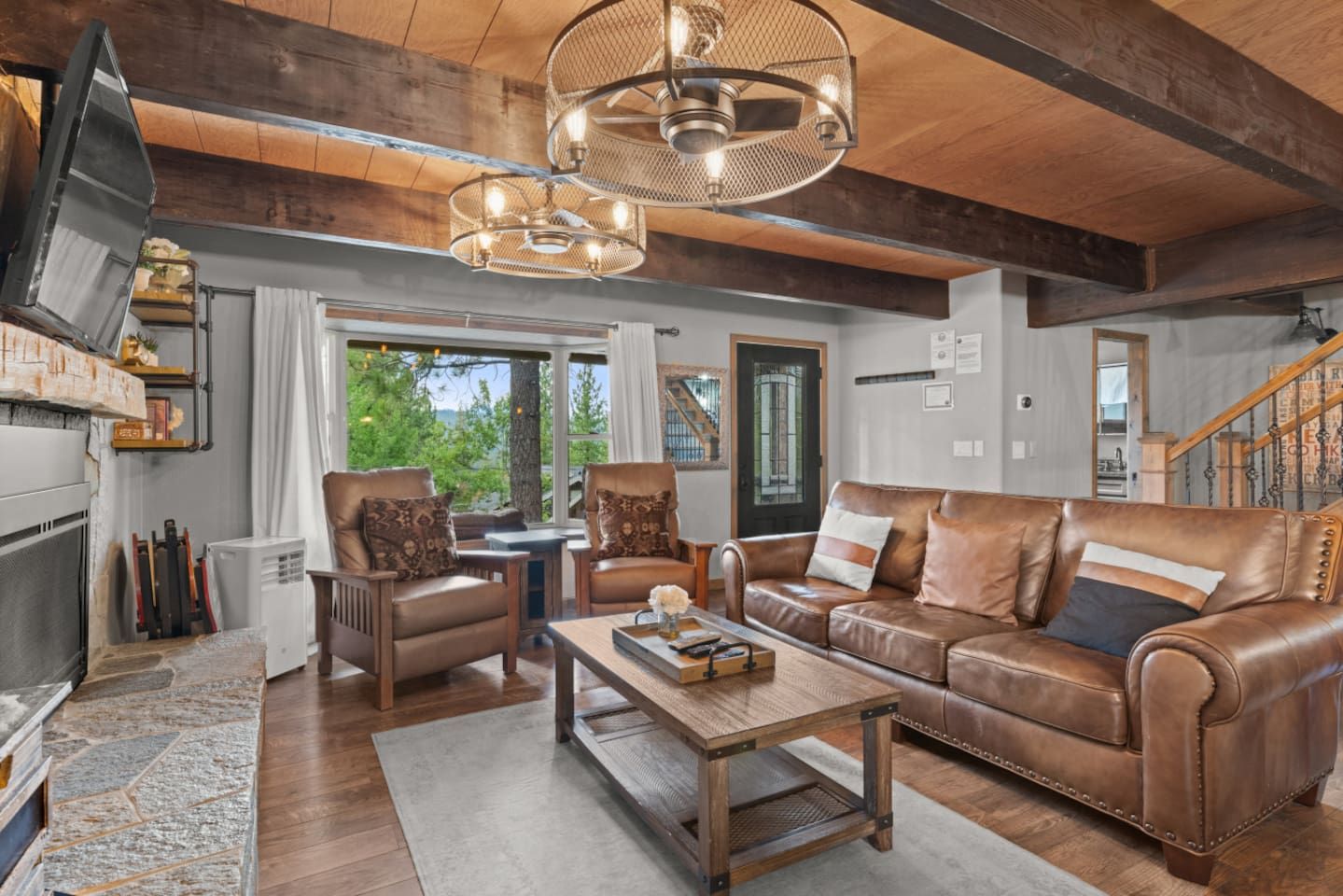 A spacious living room with a fireplace, leather sofa, wooden coffee table, and a large window offering a view of the outdoors.