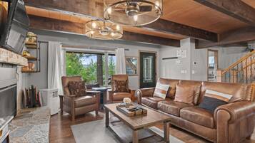 A spacious living room with a fireplace, leather sofa, wooden coffee table, and a large window offering a view of the outdoors.