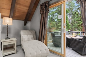 Un dormitorio con una cama individual, una mesita de noche, una lámpara y un ventanal corredero que da a una terraza exterior con mobiliario de mimbre y una chimenea.