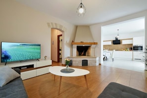 Ein modernes Wohnzimmer mit Flachbildfernseher, Kamin und einer Küche im Hintergrund.