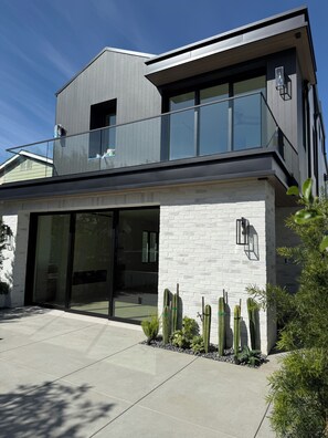 Een modern huis met twee verdiepingen, een balkon, een garage en een verzorgde tuin met cactussen.
