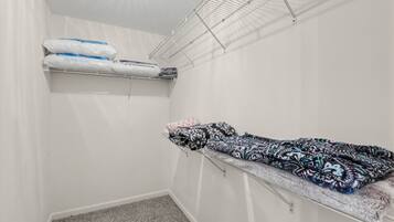 A small, white-walled room with a bunk bed, a storage shelf with pillows, and a carpeted floor.
