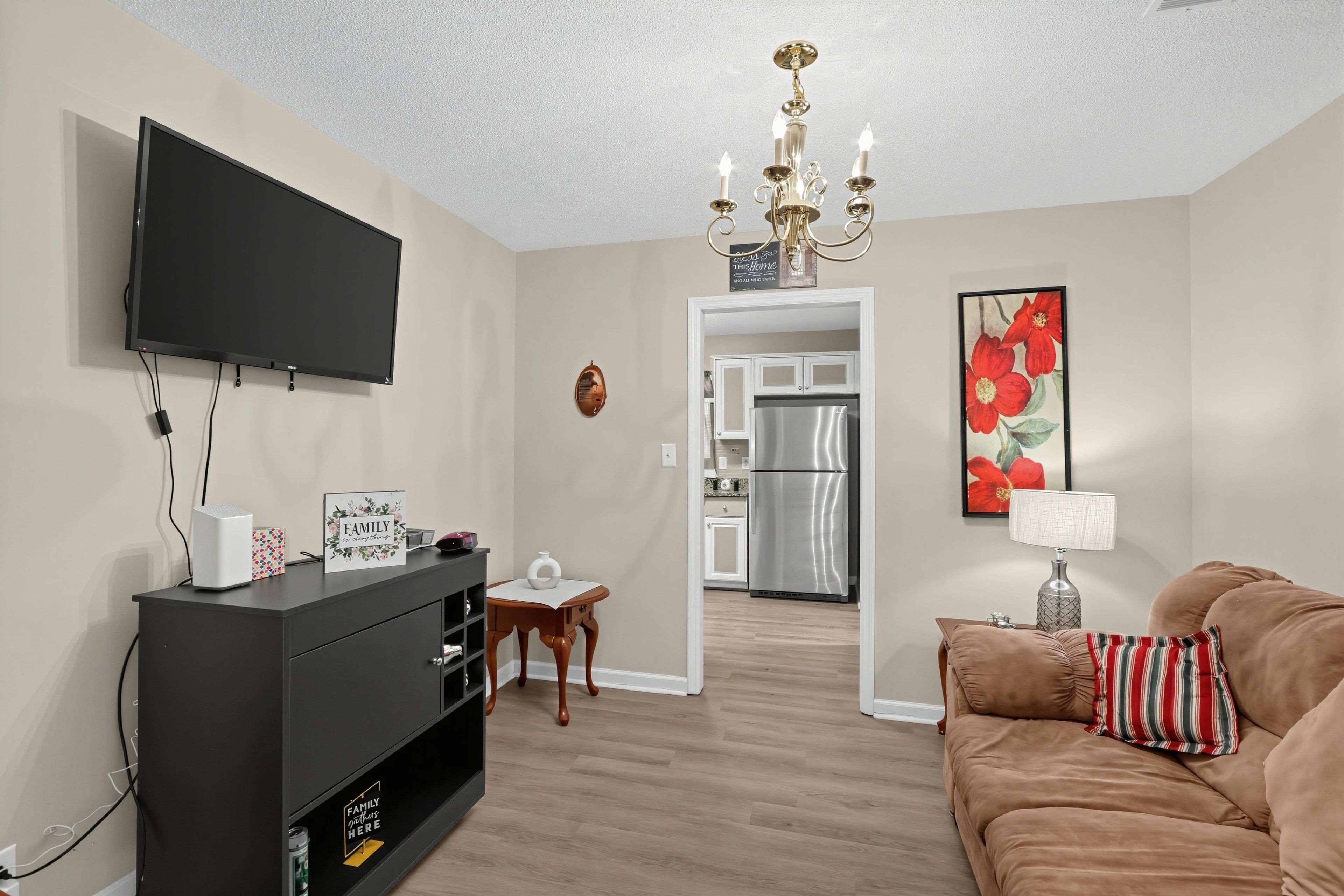 A living room with a flat-screen TV, a black entertainment unit, a brown sofa, and a red flower painting.