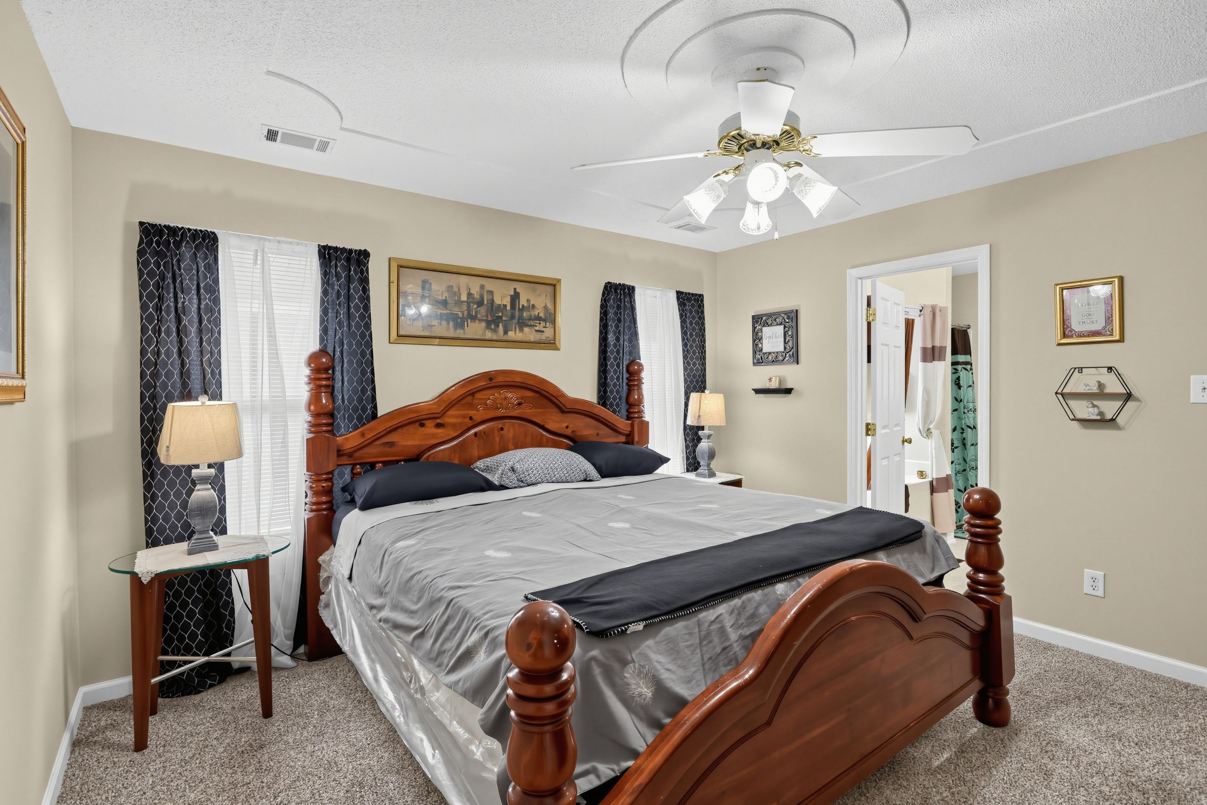 A bedroom with a wooden four-poster bed, a ceiling fan, and a cityscape painting on the wall.