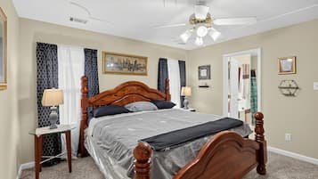A bedroom with a wooden four-poster bed, a ceiling fan, and a cityscape painting on the wall.