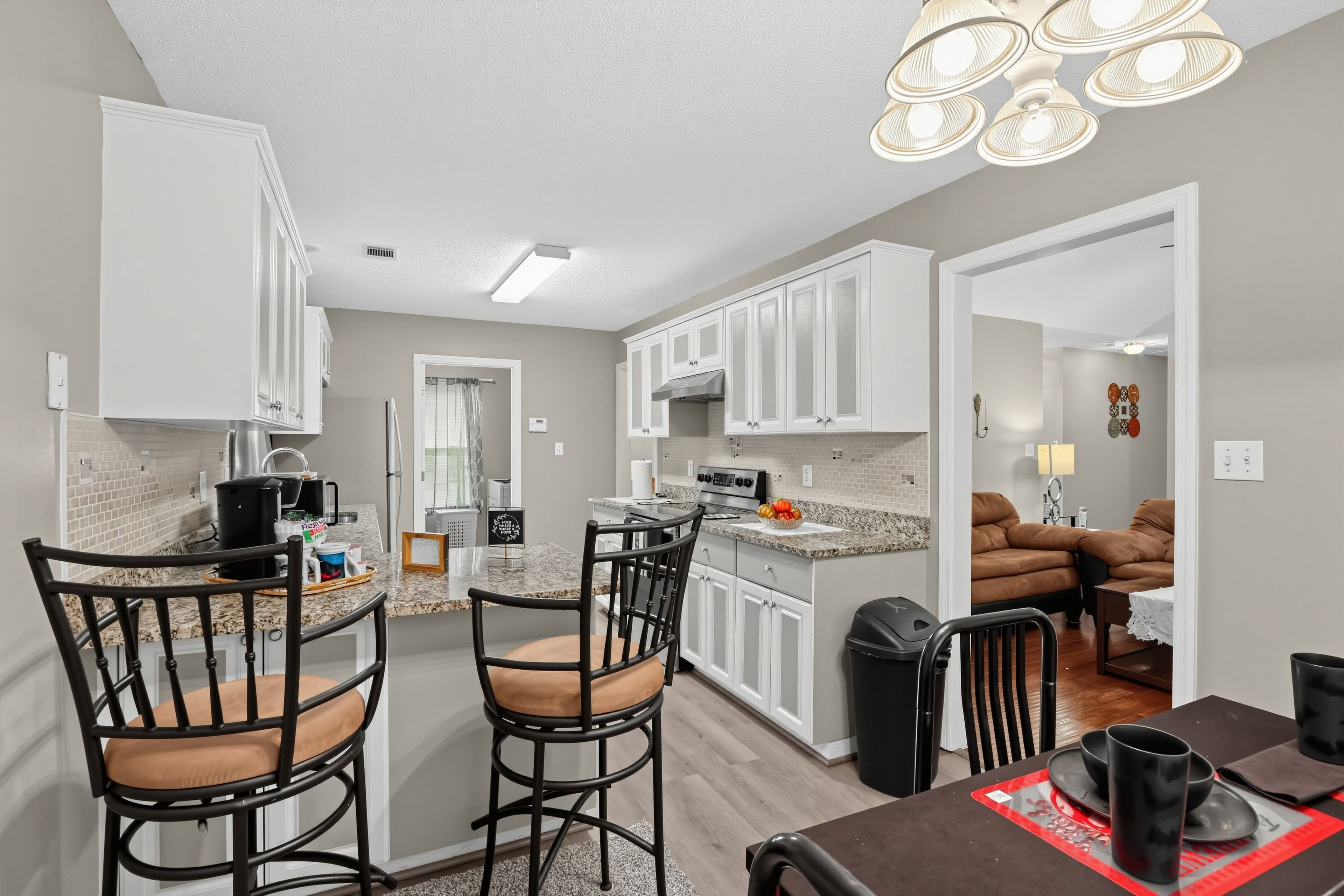 A modern kitchen with white cabinetry, a granite countertop, and a dining area with a brown table and chairs.