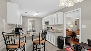 A modern kitchen with white cabinetry, a granite countertop, and a dining area with a brown table and chairs.