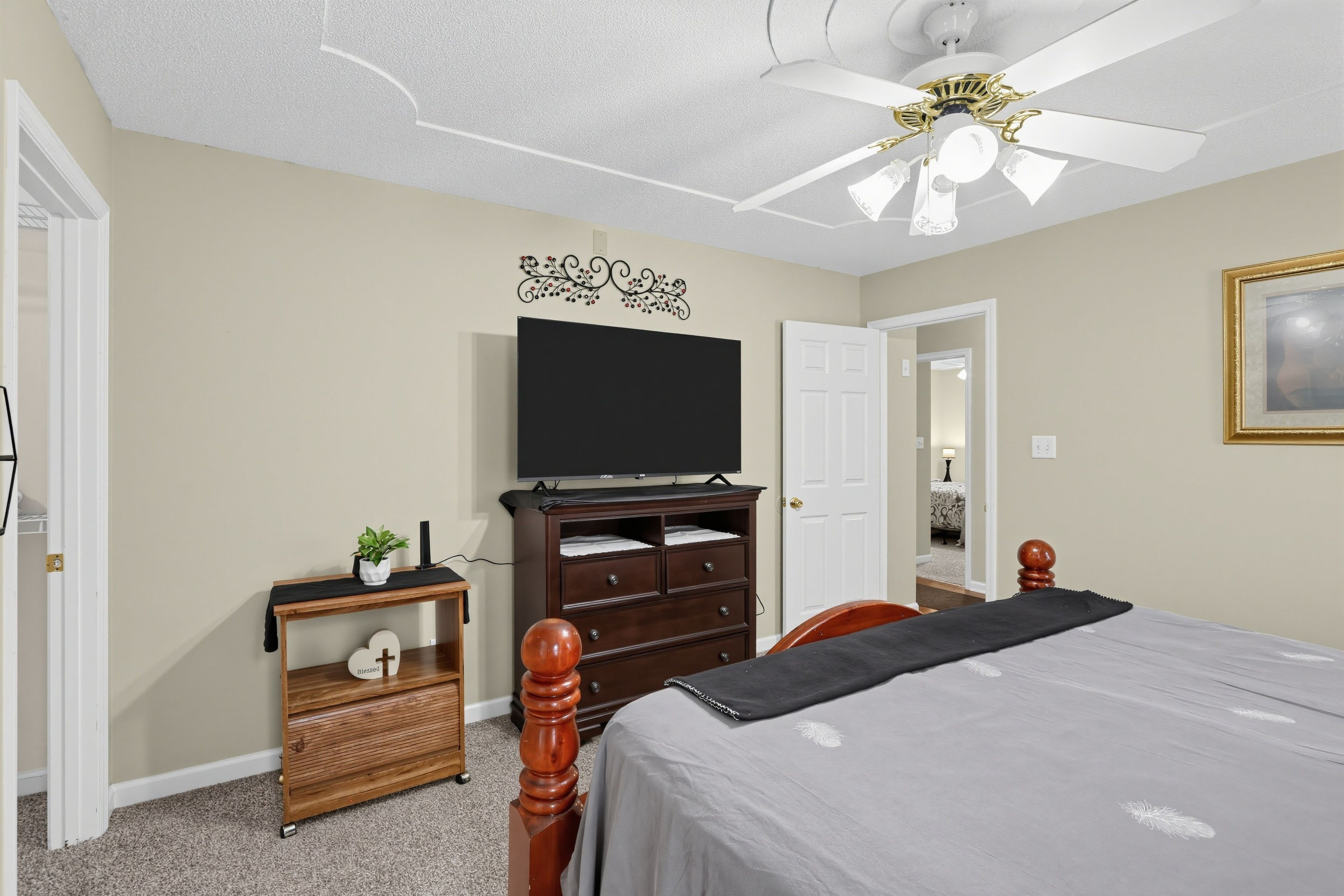 A bedroom with a bed, a dresser, a television, and a ceiling fan.