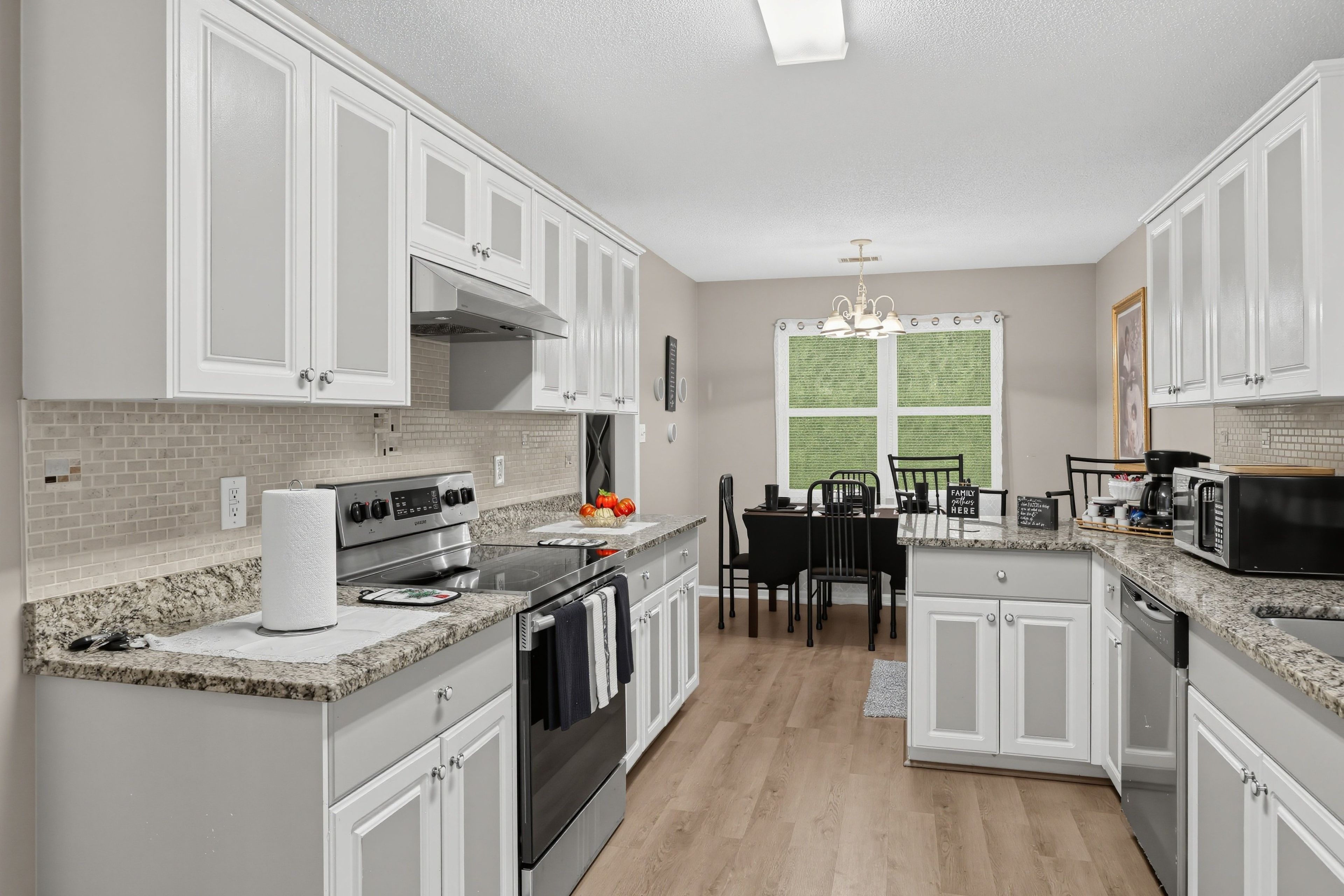 A kitchen with white cabinetry, a stainless steel stove, a microwave, and a dining area with a table and chairs.