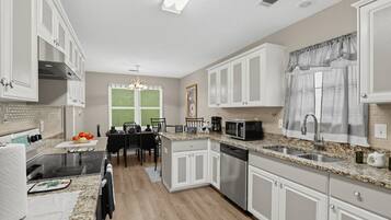 A modern kitchen with white cabinetry, a granite countertop, stainless steel appliances, and a dining area with a table and chairs.