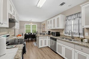 A modern kitchen with white cabinetry, a granite countertop, stainless steel appliances, and a dining area with a table and chairs. - Hephzibah Unique Comfortable 4br Retreat For 8 4 Bedroom Home (Hephzibah)