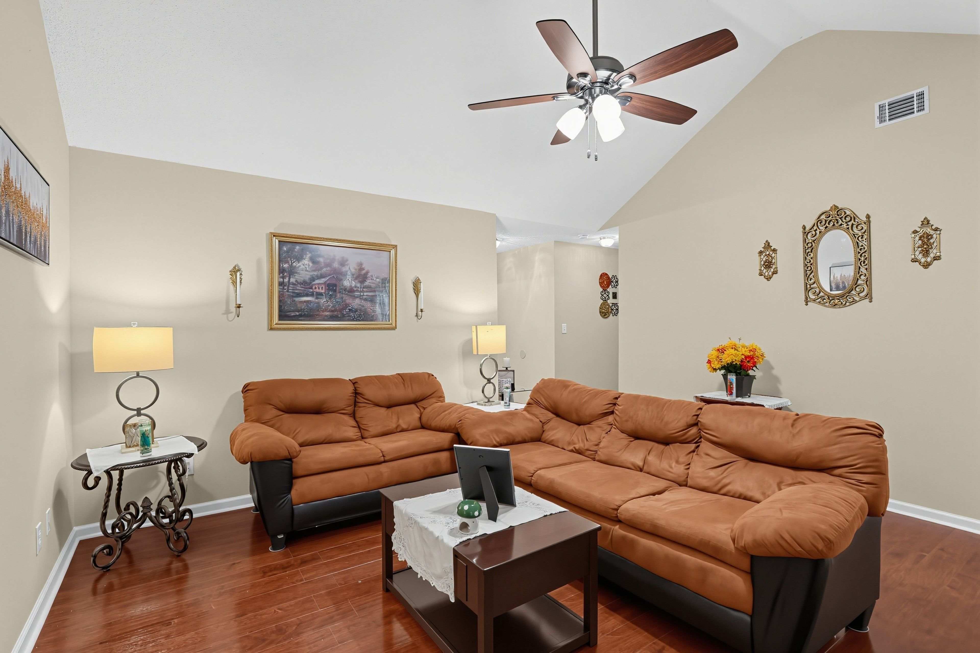 A living room with a brown leather sectional sofa, a coffee table, a ceiling fan, and a painting on the wall.