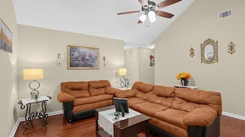 A living room with a brown leather sectional sofa, a coffee table, a ceiling fan, and a painting on the wall.