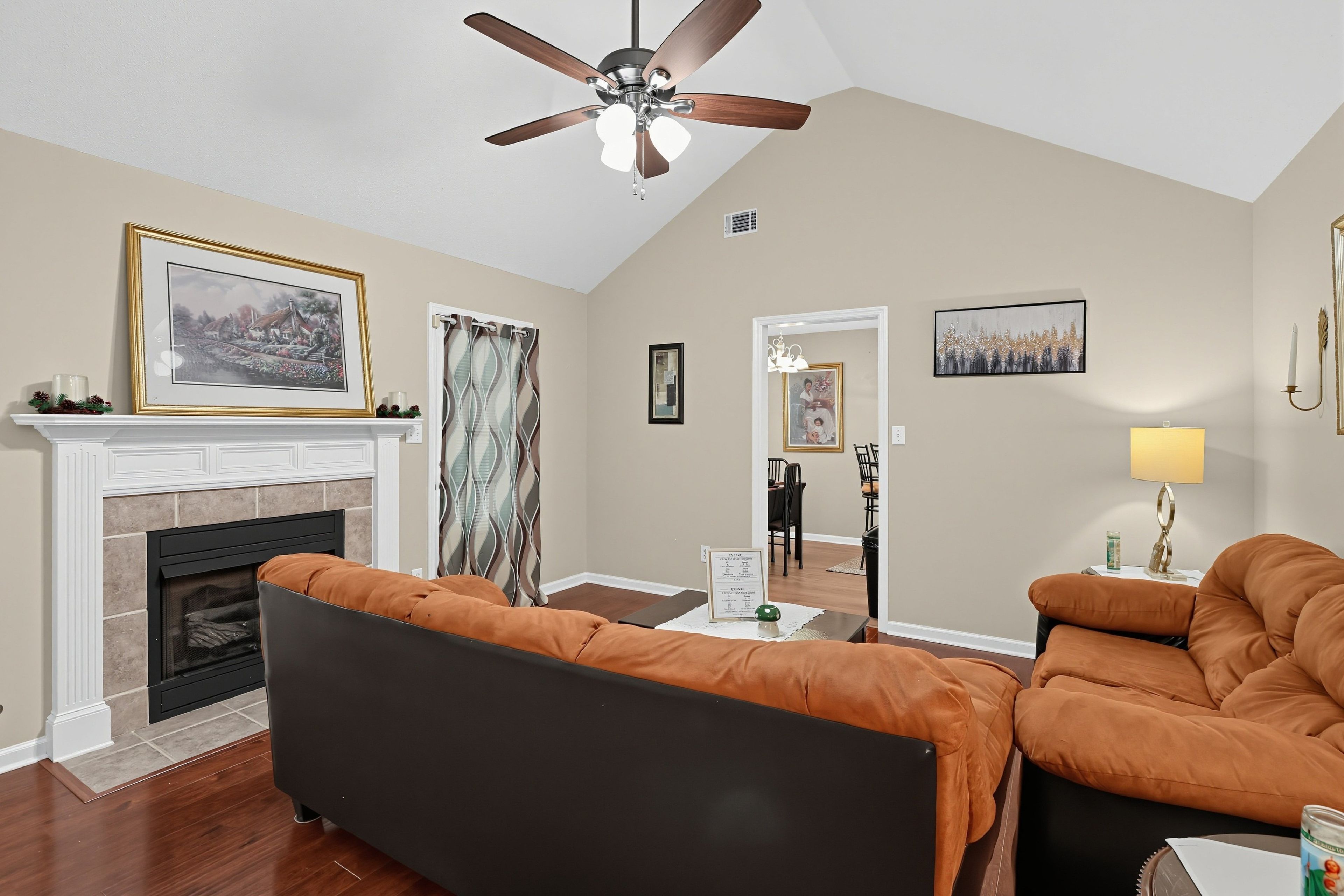 A living room with a fireplace, a ceiling fan, and a dining area with chairs.