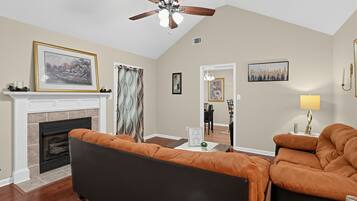 A living room with a fireplace, a ceiling fan, and a dining area with chairs.