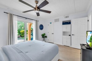 Ein Schlafzimmer mit einem Bett, einem Deckenventilator, einer Uhr, einer Tür und einem Fernseher.