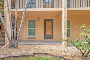 Ein zweistöckiges Gebäude mit einer beige farbenen Fassade, einer dunkel gefärbten Tür mit der Nummer 123 und einem kleinen Gartenbereich mit Kieselsteinen und einigen Pflanzen.