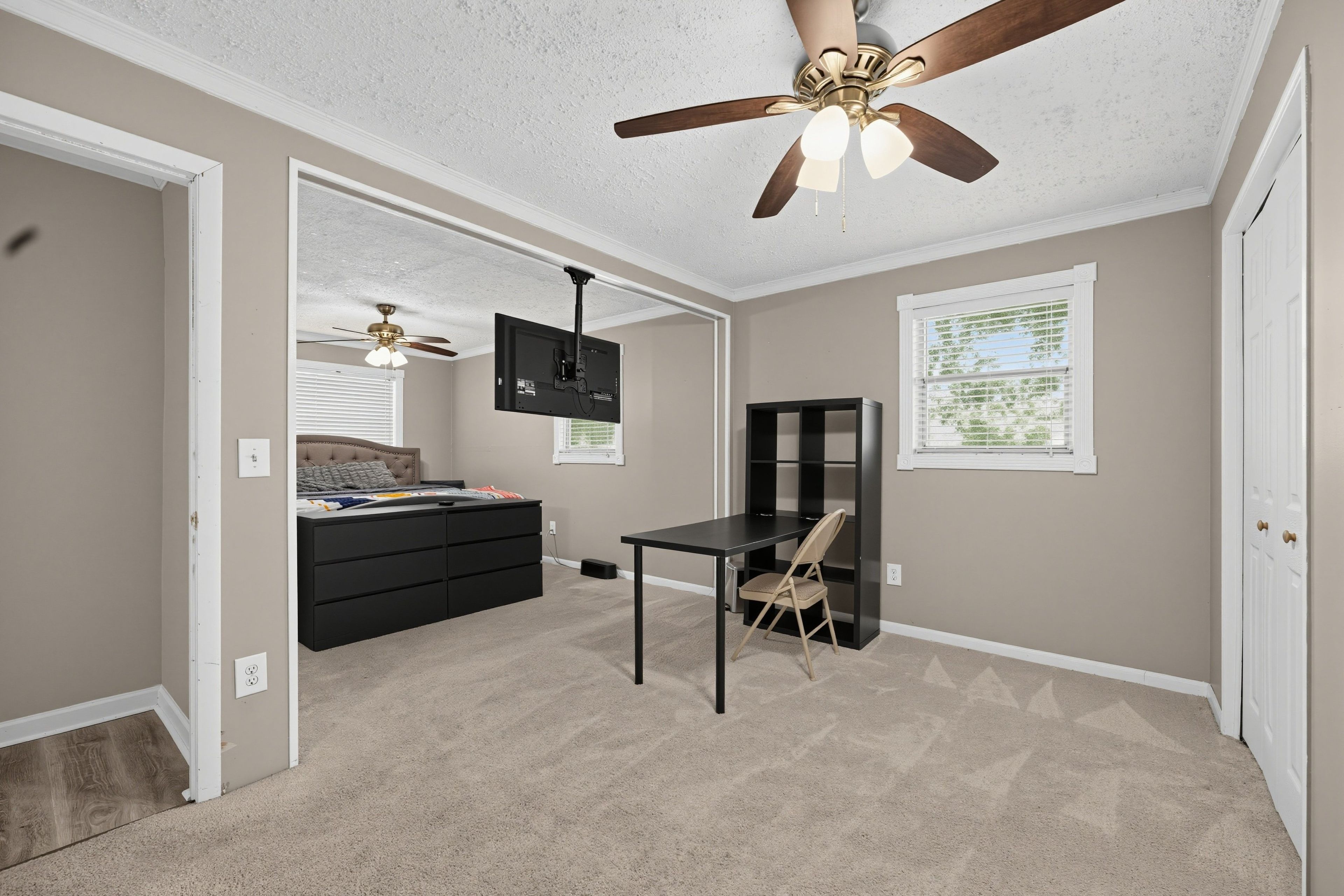 A bedroom with a bed, a desk, a chair, a ceiling fan, and a window.
