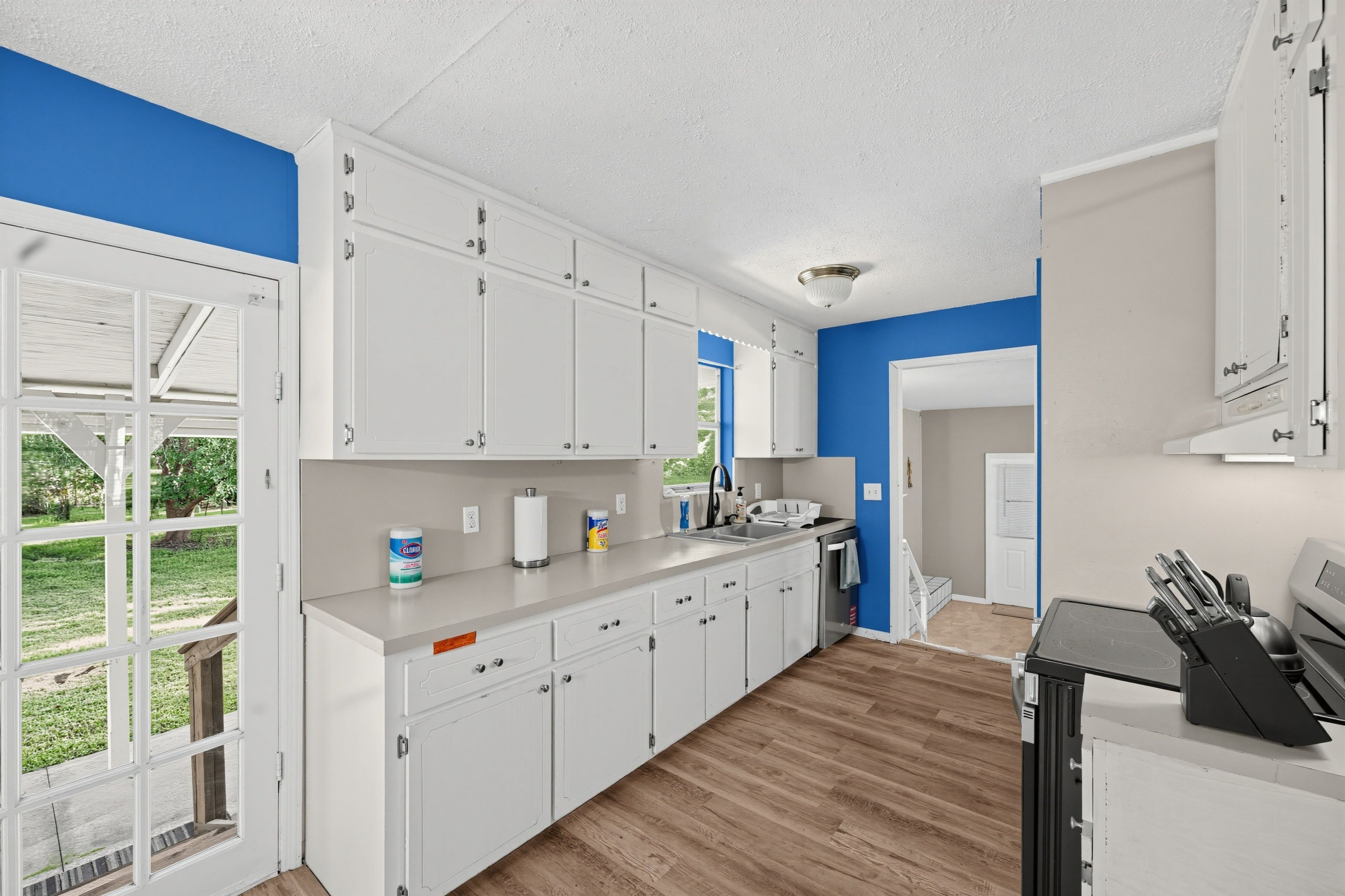 A kitchen with white cabinets, a countertop, and a view of the outdoors.