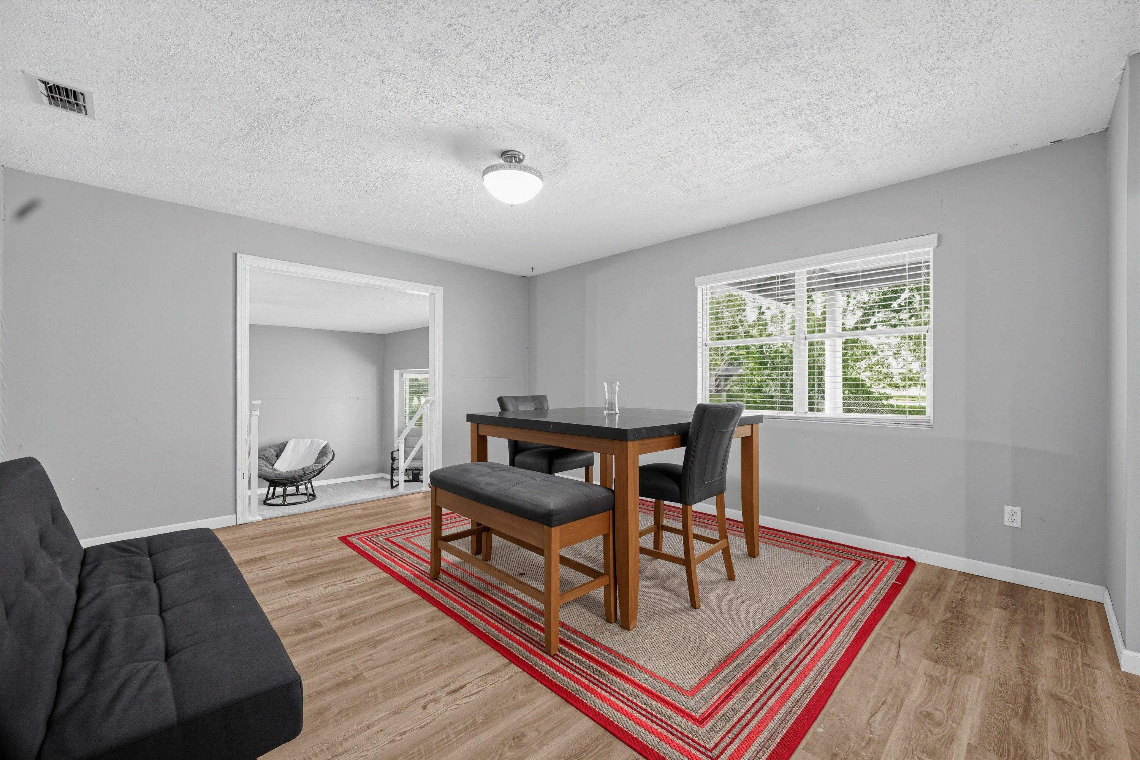 A modern living room with a dining area, hardwood flooring, and a view of greenery through the window.