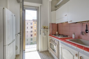 A kitchen with a gas stove, oven, and sink. There is a window with a view of buildings outside. - 10 Via Cadibona – Living Milano (Milan)