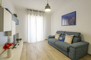 A living room with a grey sofa, a flat-screen TV, a vase with flowers, and a painting on the wall. - 10 Via Cadibona – Living Milano (Milan)