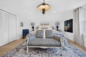 A bedroom with a bed, bedside tables, a chair, a hanging light fixture, and a large window with curtains. - La Laval At Winyah Bay Main And Guest House 8 Bedroom Home (Georgetown)