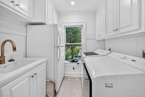 A compact kitchen with white cabinetry, a stainless steel sink, a built-in oven, and a window providing a view of greenery. - La Laval At Winyah Bay Main And Guest House 8 Bedroom Home (Georgetown)