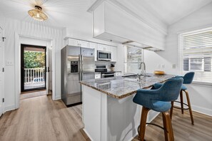 A modern kitchen with white cabinetry, a stainless steel refrigerator, a built-in oven, and a marble countertop. - 146-3 Par For Pawleys 2 Bedroom Condo (Pawleys Island)