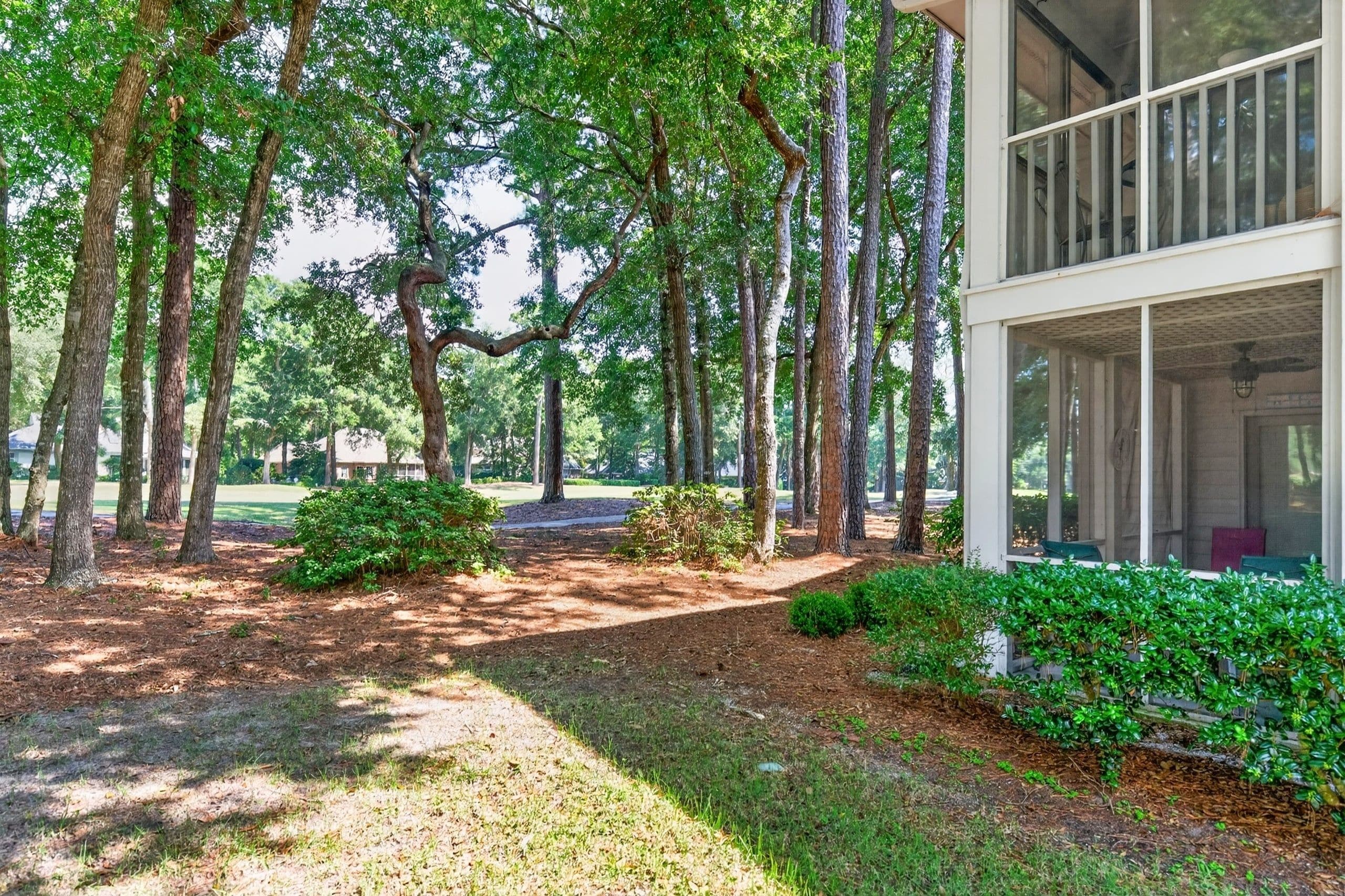 A building with a covered porch, surrounded by a wooded area with a dirt path leading to it.