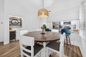 A modern kitchen with stainless steel appliances, a dining area with a round table and white chairs, and a hanging pendant light. - 146-3 Par For Pawleys 2 Bedroom Condo (Pawleys Island)