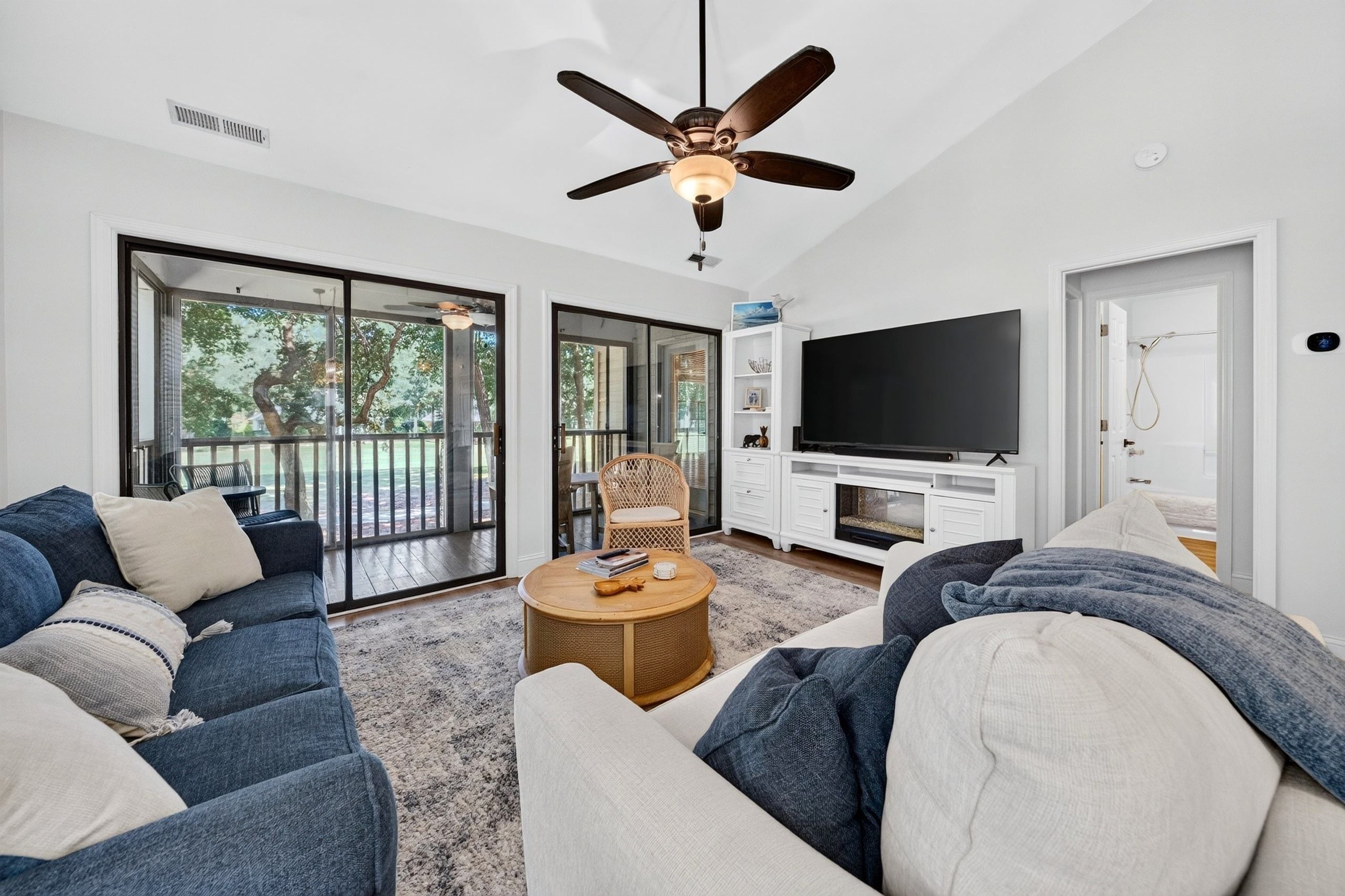 A modern living room with a large flat-screen TV, a ceiling fan, and a sliding glass door leading to an outdoor area.