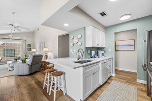 A modern kitchen with white cabinetry, a central island with stools, and a dining area with a sofa and chairs. - Seascape Villa 14D *Updated*Modern*Beach access* (Miramar Beach)