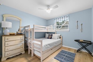 Ein Schlafzimmer mit Etagenbett, Kommode, Schreibtisch und Deckenventilator.