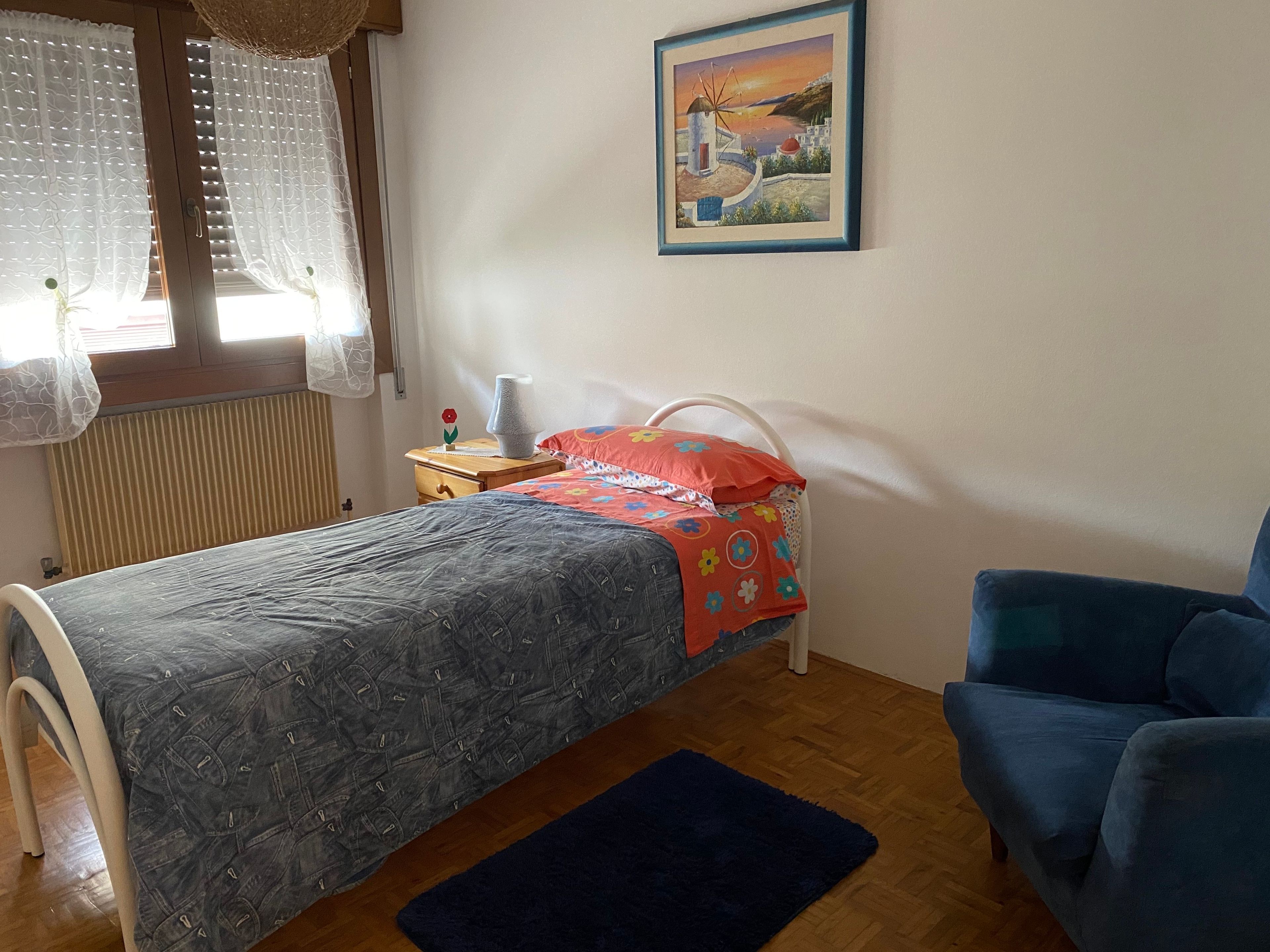 Ein Schlafzimmer mit einem Bett, einem Sessel, einem Nachttisch, einer Lampe und einem Bild an der Wand.