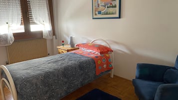 Ein Schlafzimmer mit einem Bett, einem Sessel, einem Nachttisch, einer Lampe und einem Bild an der Wand.