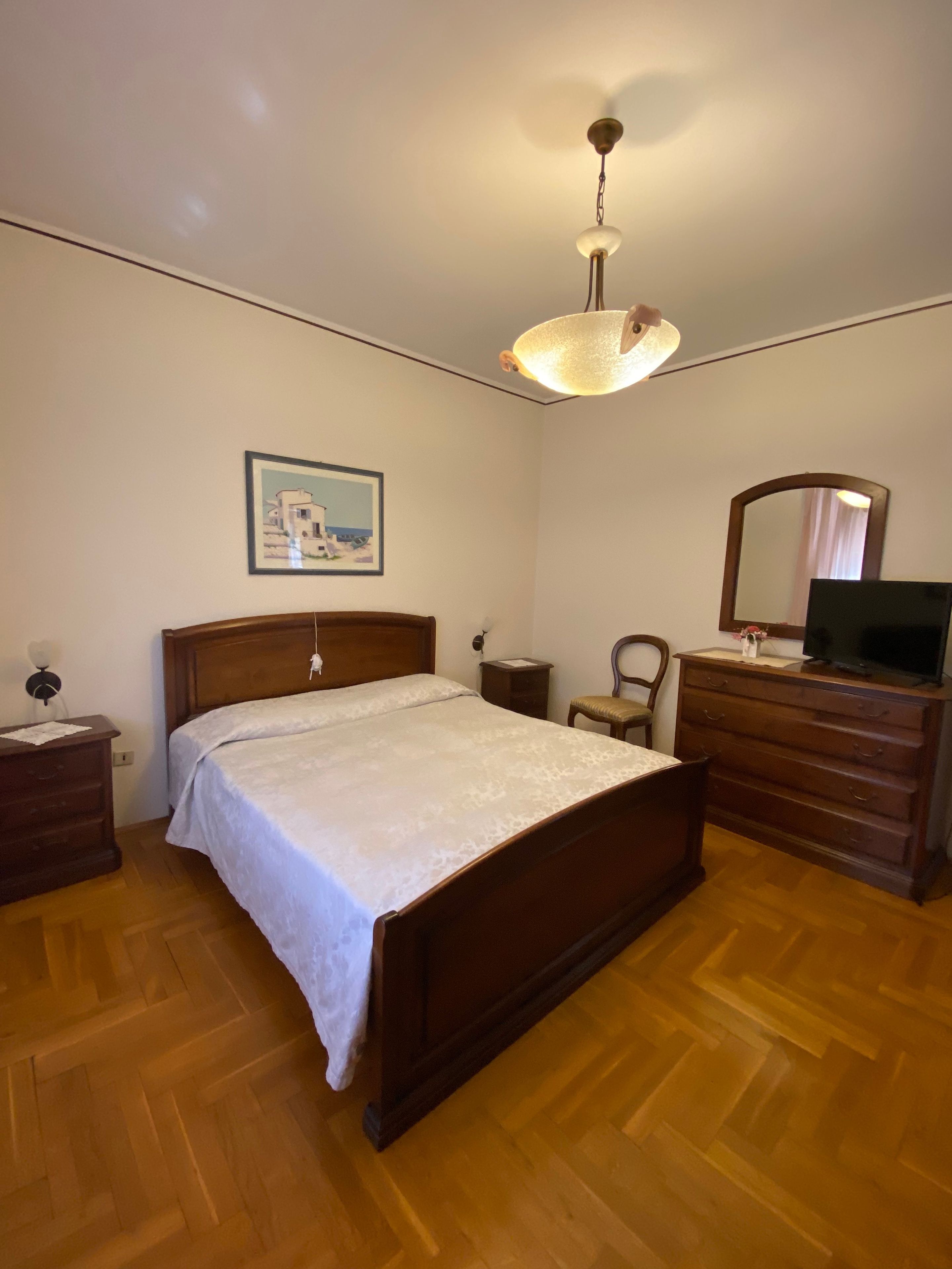 Un dormitorio con una cama de madera, un aparador, una silla, un escritorio, un espejo y una lámpara colgante.