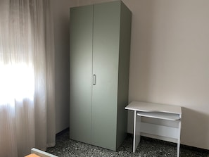 Una habitación con armario, escritorio y ventana con cortinas.
